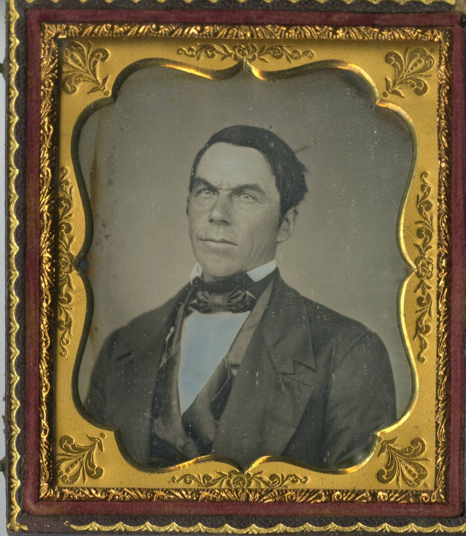 Black and white daguerreotype photographic portrait of a man from the chest up. Metal case border around the image.
